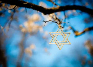 Gold Jewish star pendant hanging from a tree branch on a clear sky day