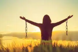Girl in a wheat field with her arms up in the air with broken chains