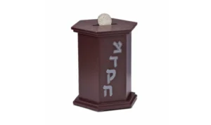 A brown Tzeduka box, that has the word tzeduka written in Hebrew with a coin getting dropped in
