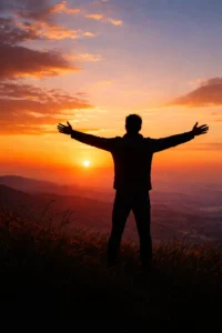 Man standing high with is arms open as the sun is setting