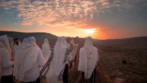 Men together listening to one blow the shofar as sun is setting