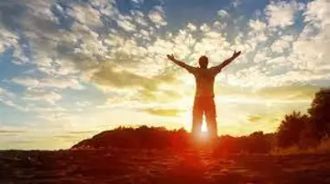 Man standing high with is arms open as the sun is setting