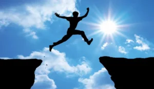 Man jumping from one cliff to another with sun shinning in the sky