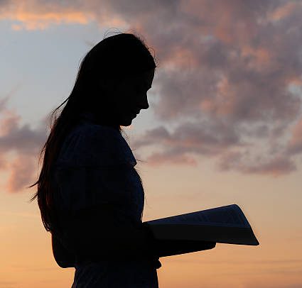Silhouette of a young girl reading from bible in sunset light.Please feel invited to view my photos from lightboxex!