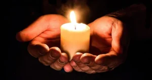 Hands together holding a lit white candle