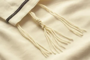 Close-up of tzitzit fringes tied in traditional knots on the corner of a tallit, resting on soft white fabric
