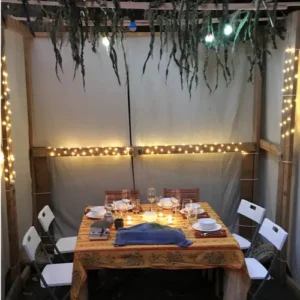 Picture of a table and chairs set in a sukah with lights around the side