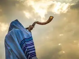 Jewish man in a tallit prayer shawl blowing the shofar