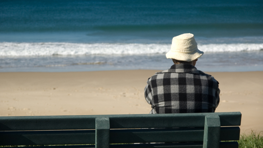 Man sitting on a bench by the beach watching the waves