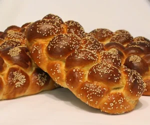 Two braided challahs, stacked in a x shape, with sesame topping